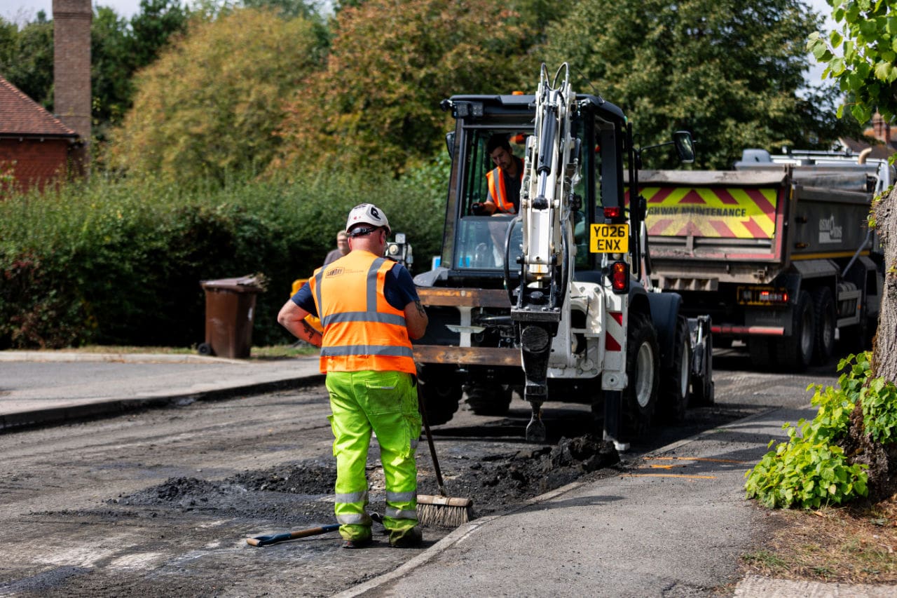 Lawday operative sweeping alongside excavator and delivery truck on a residential street